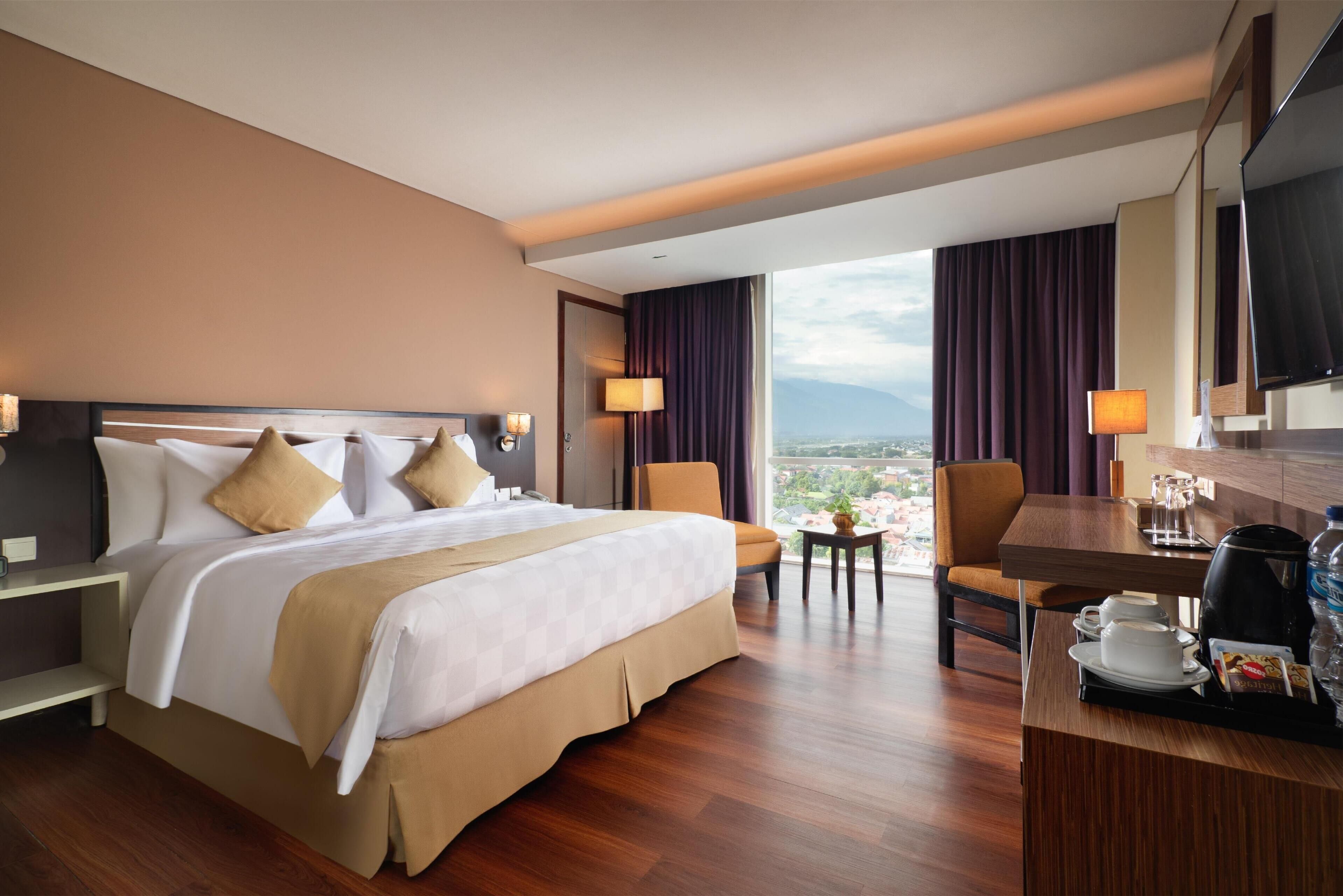 Habitación de hotel con una cama grande, un escritorio con cafetera y vistas a la ciudad.
