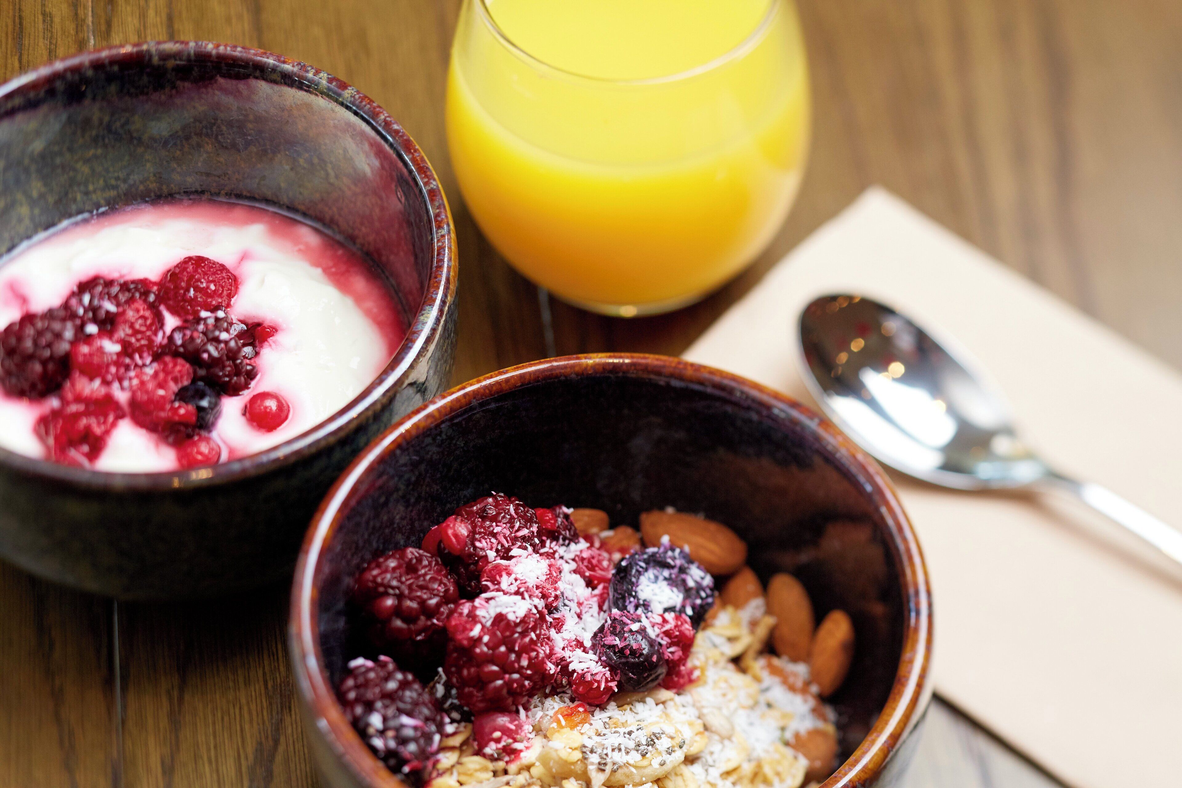 Two bowls of food with berries and a glass of orange juice on a wooden table.