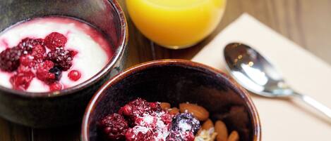 Two bowls of food with berries and a glass of orange juice on a wooden table.