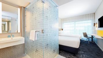 Habitación de hotel con cabina de ducha de vidrio, cama, escritorio, silla y televisor.