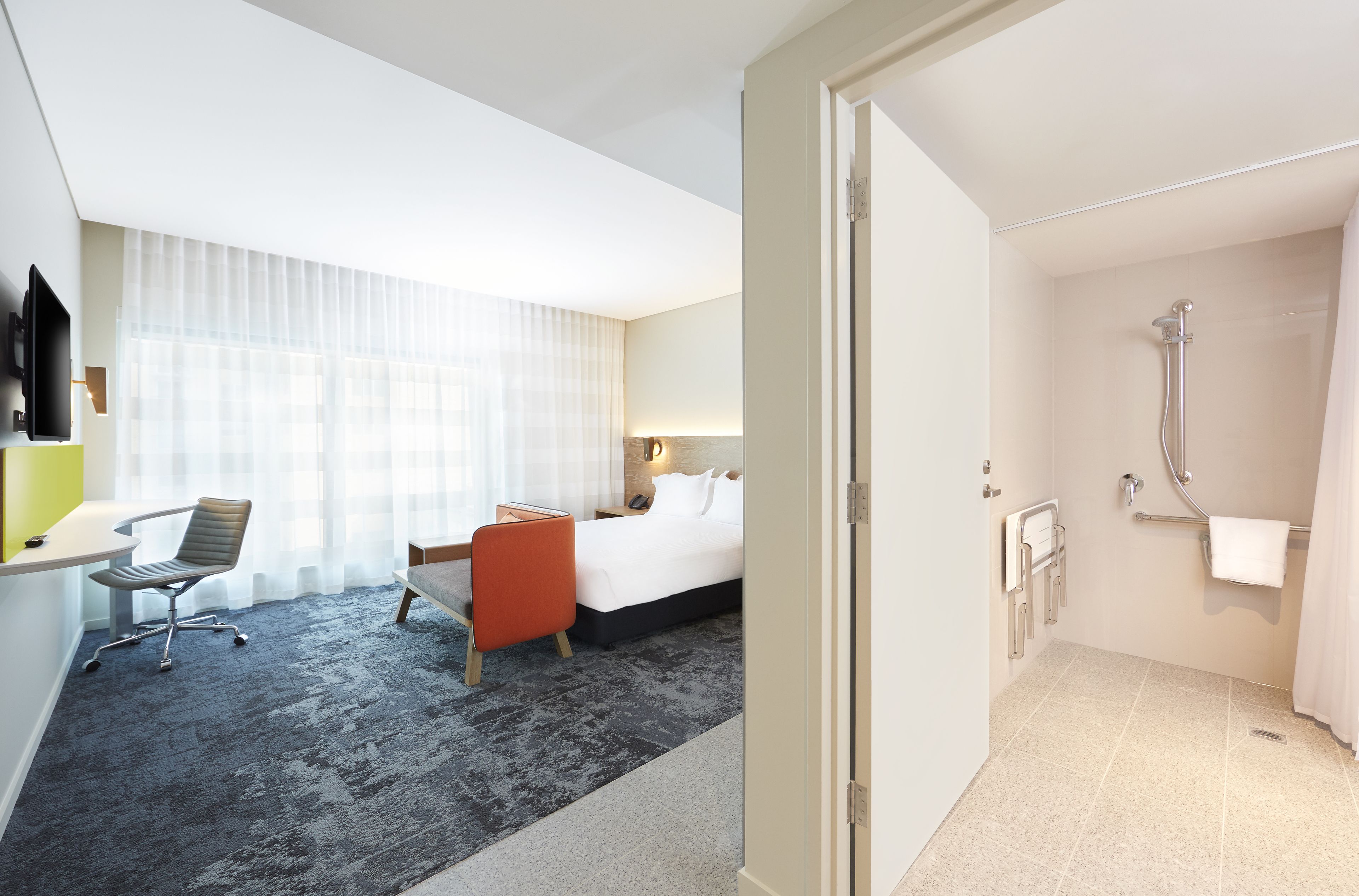 A hotel room with a bed, desk, chair, and a shower area.