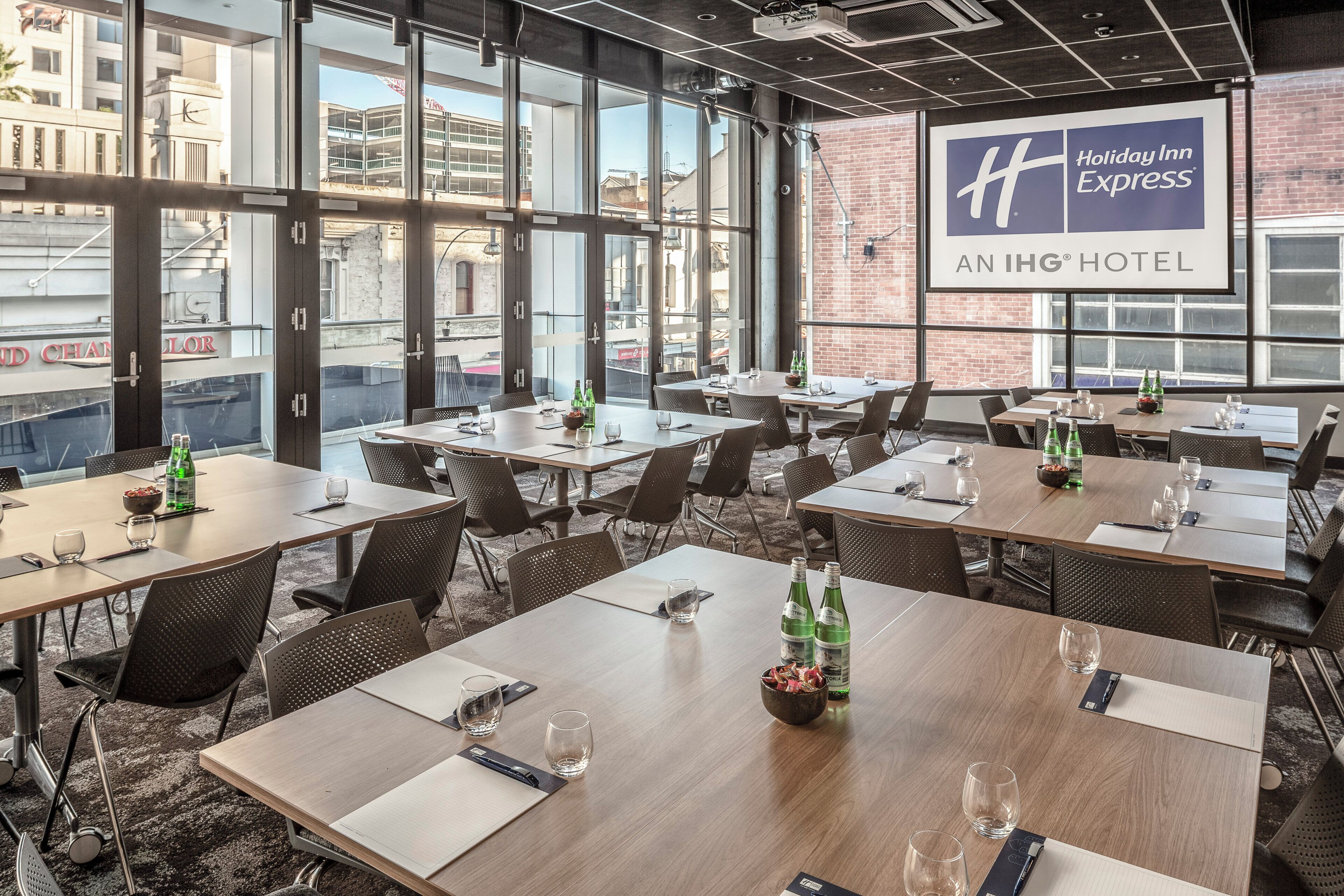 A conference room with multiple tables and chairs, large windows with a view of buildings, and a Holiday Inn Express sign.