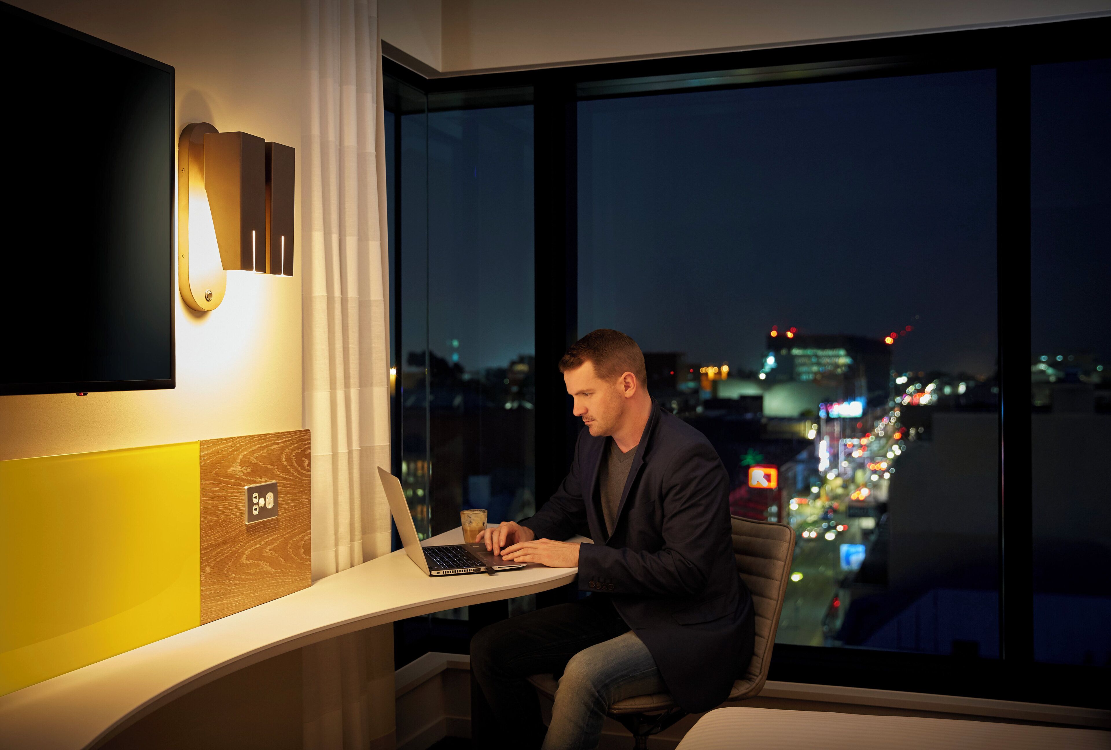A man working on a laptop at a desk with a city view.