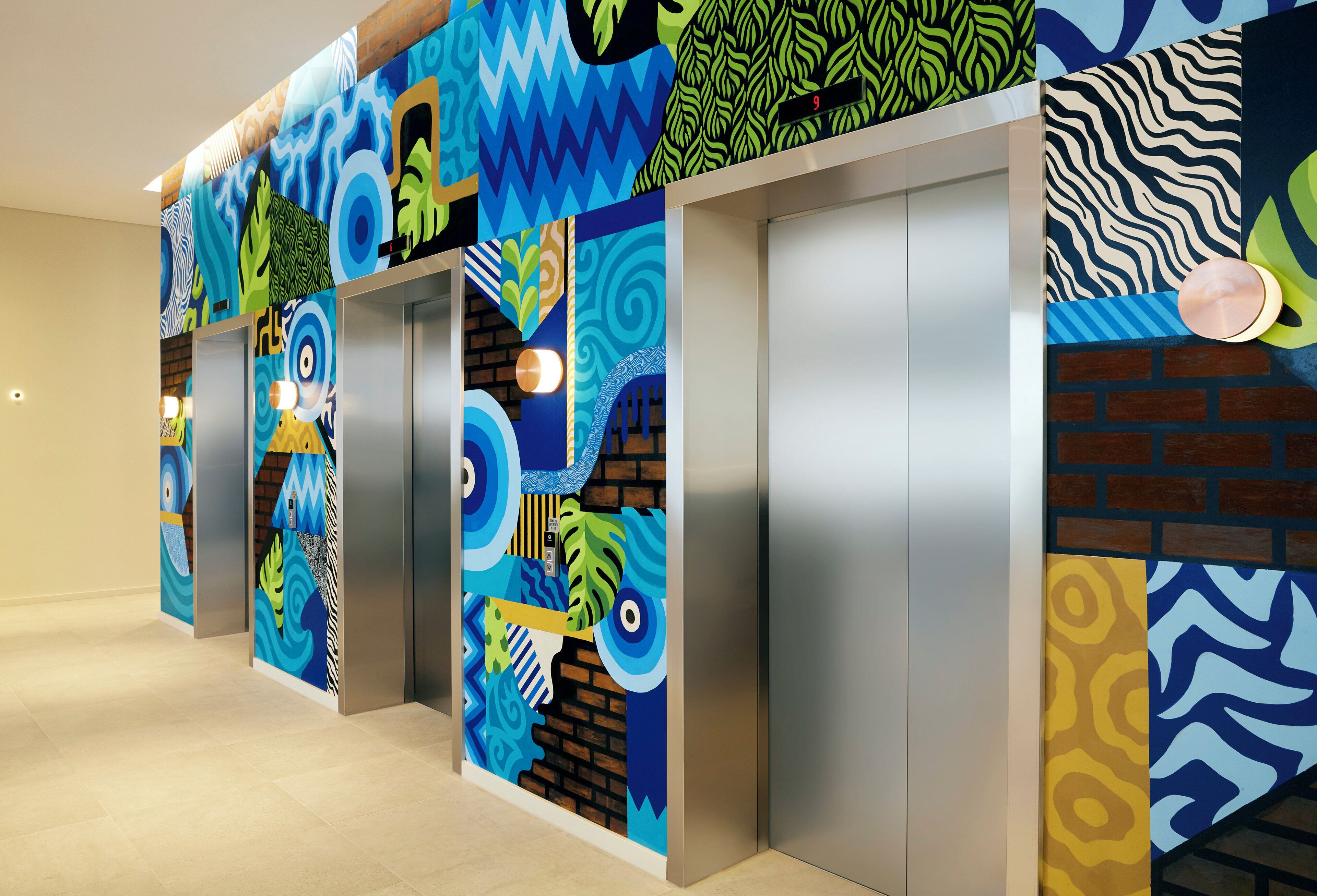 A hallway with elevators, each with a unique colorful wall design.