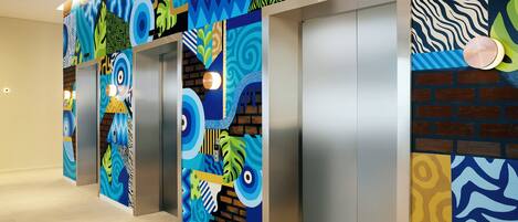 A hallway with elevators, each with a unique colorful wall design.