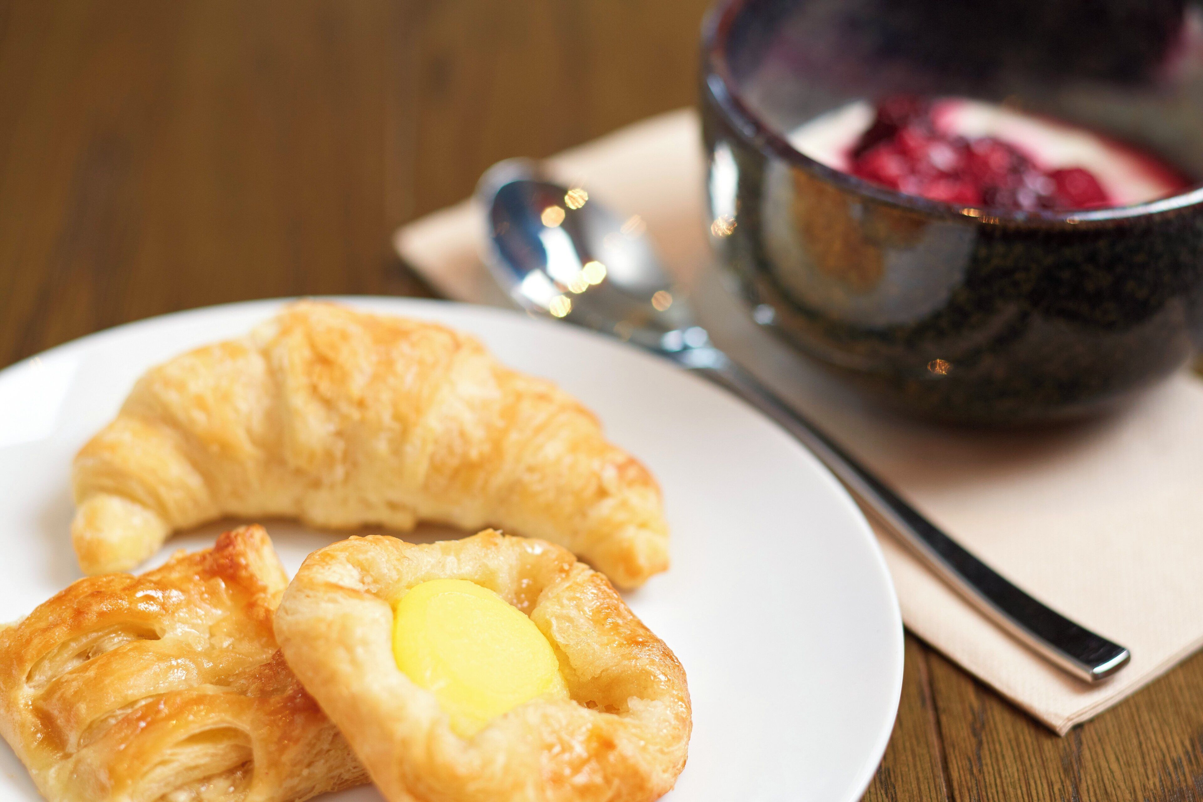 A plate with two pastries and a bowl of berries on a wooden table.