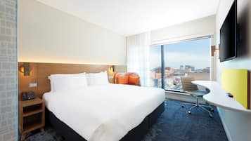 A hotel room with a large bed, a desk with a chair, a flat-screen TV, and a city view.