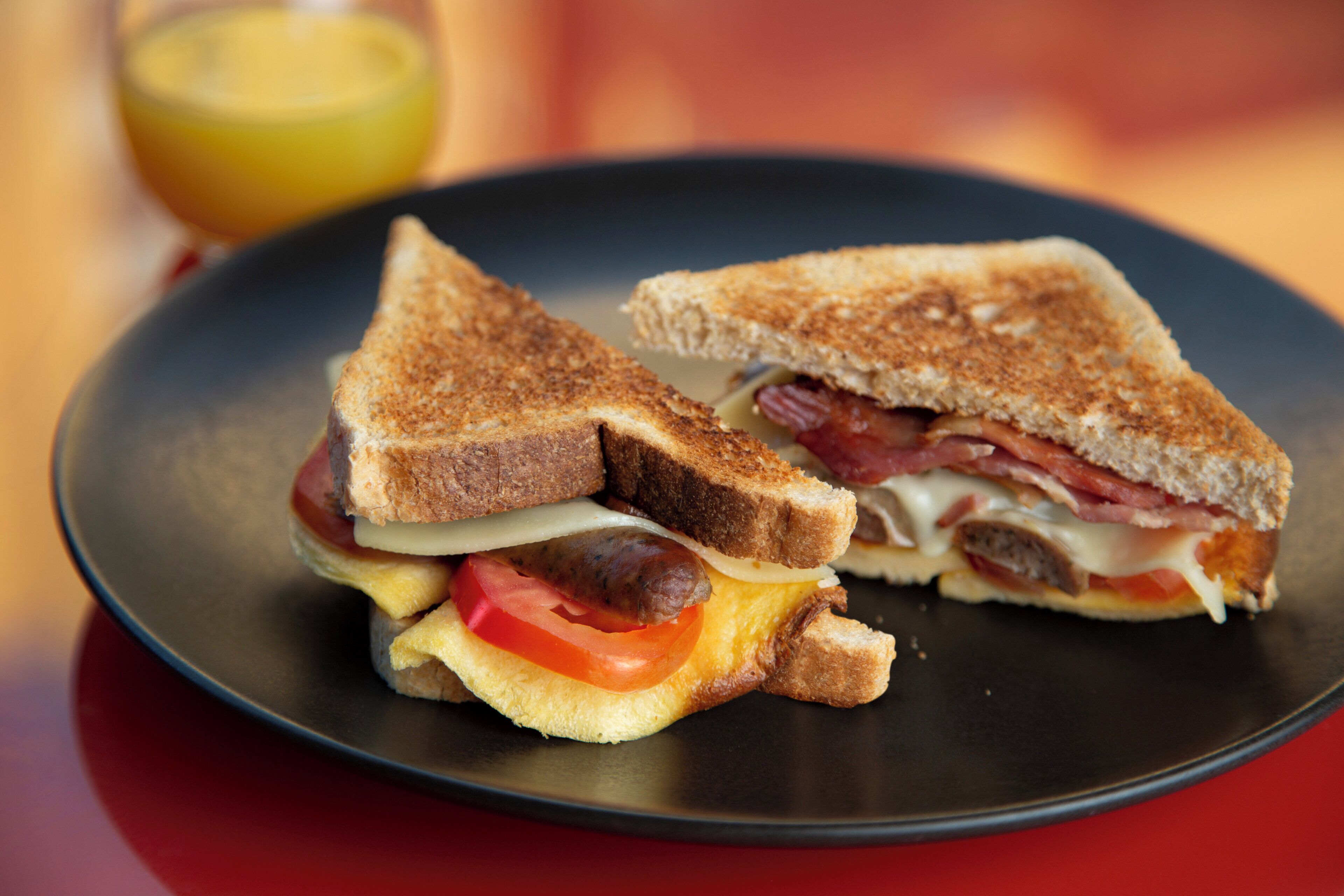 A sandwich cut in half on a plate, with visible ingredients like bacon, cheese, and tomato.