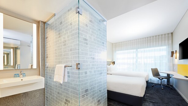 A hotel room with a glass shower enclosure, a bed, a desk, and a TV mounted on the wall. - Holiday Inn Express Adelaide City Centre by IHG (Adelaide)