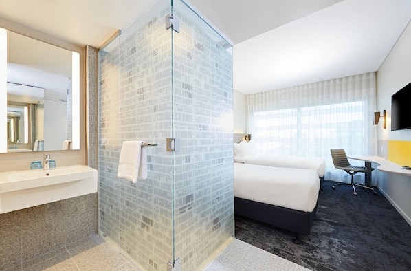 Une chambre d’hôtel dotée d’une douche en verre, d’un lit, d’un bureau et d’un téléviseur fixé au mur.