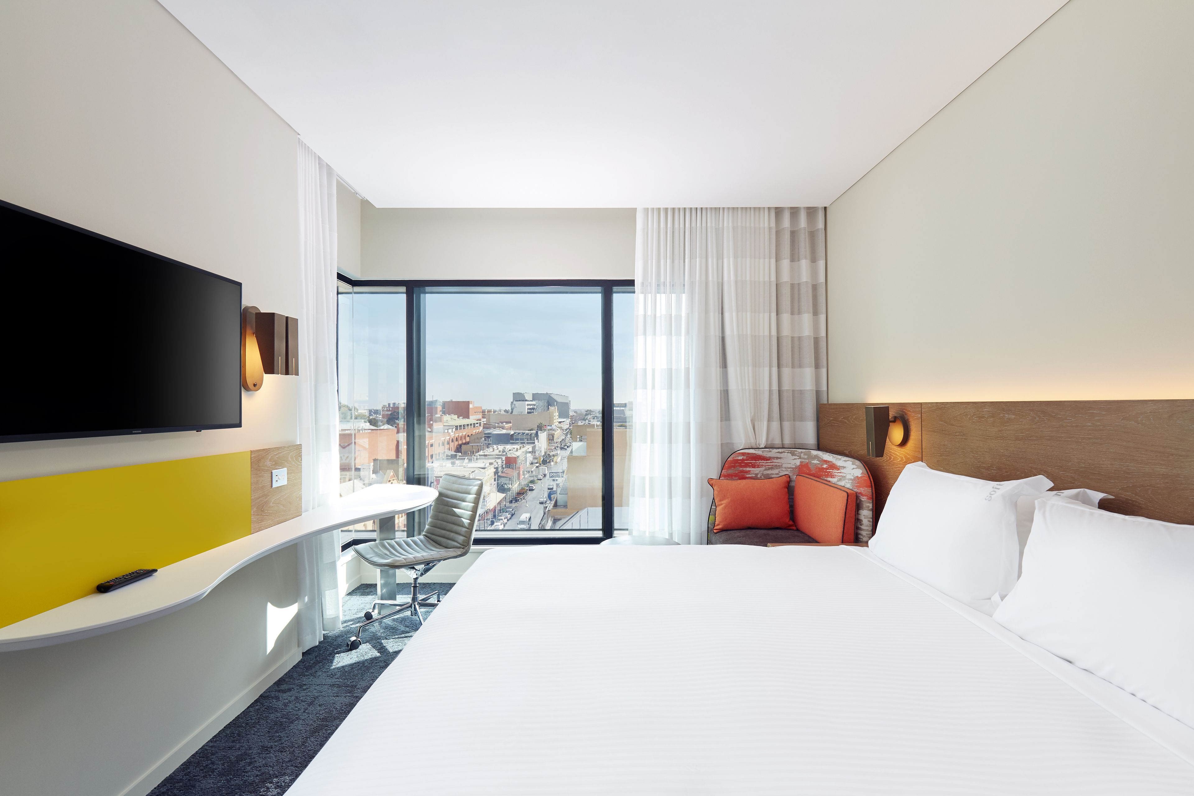 Habitació d'hotel amb llit, televisió, escriptori i vista a la ciutat.