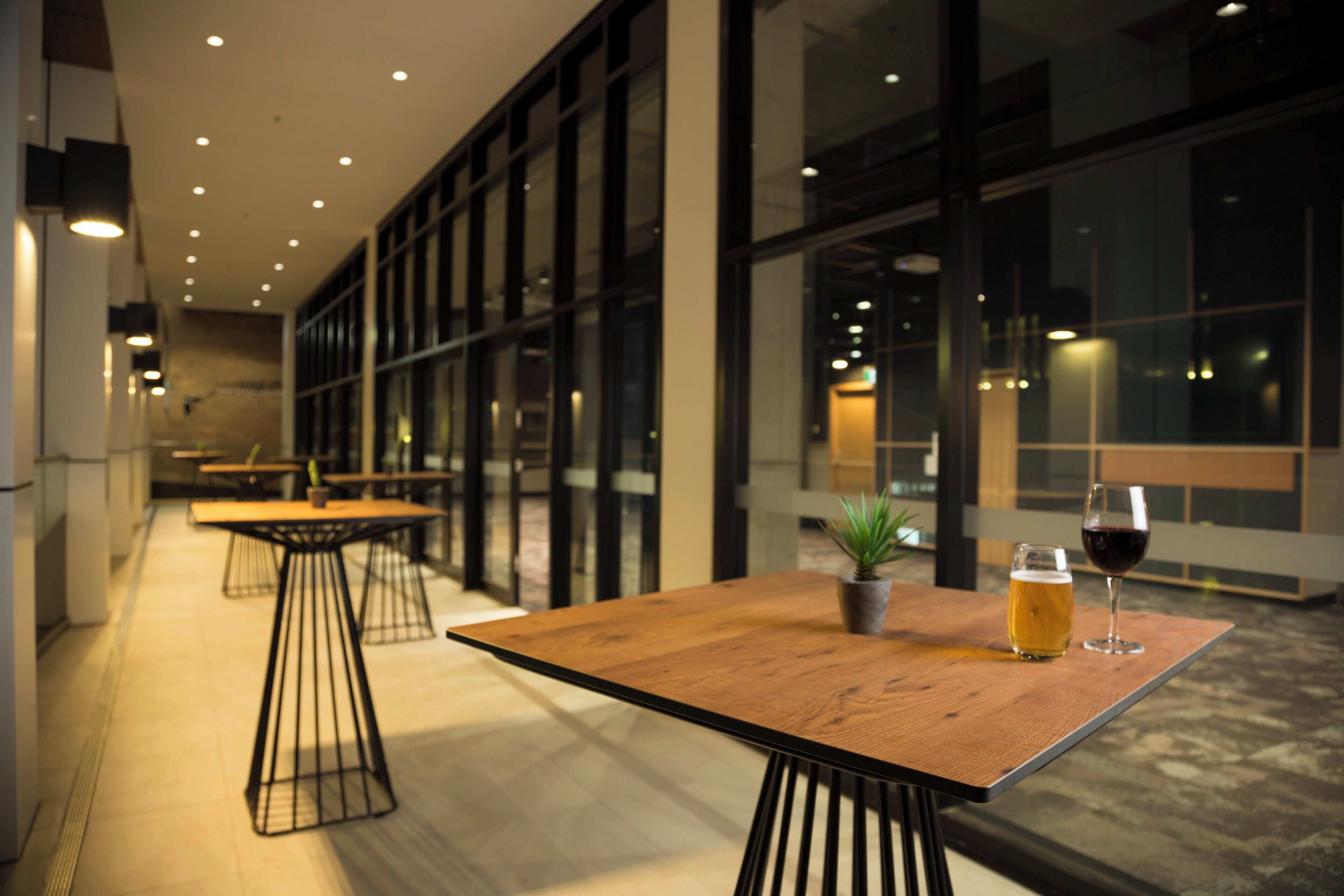 An indoor seating area with tables and chairs, a glass partition, and a potted plant.