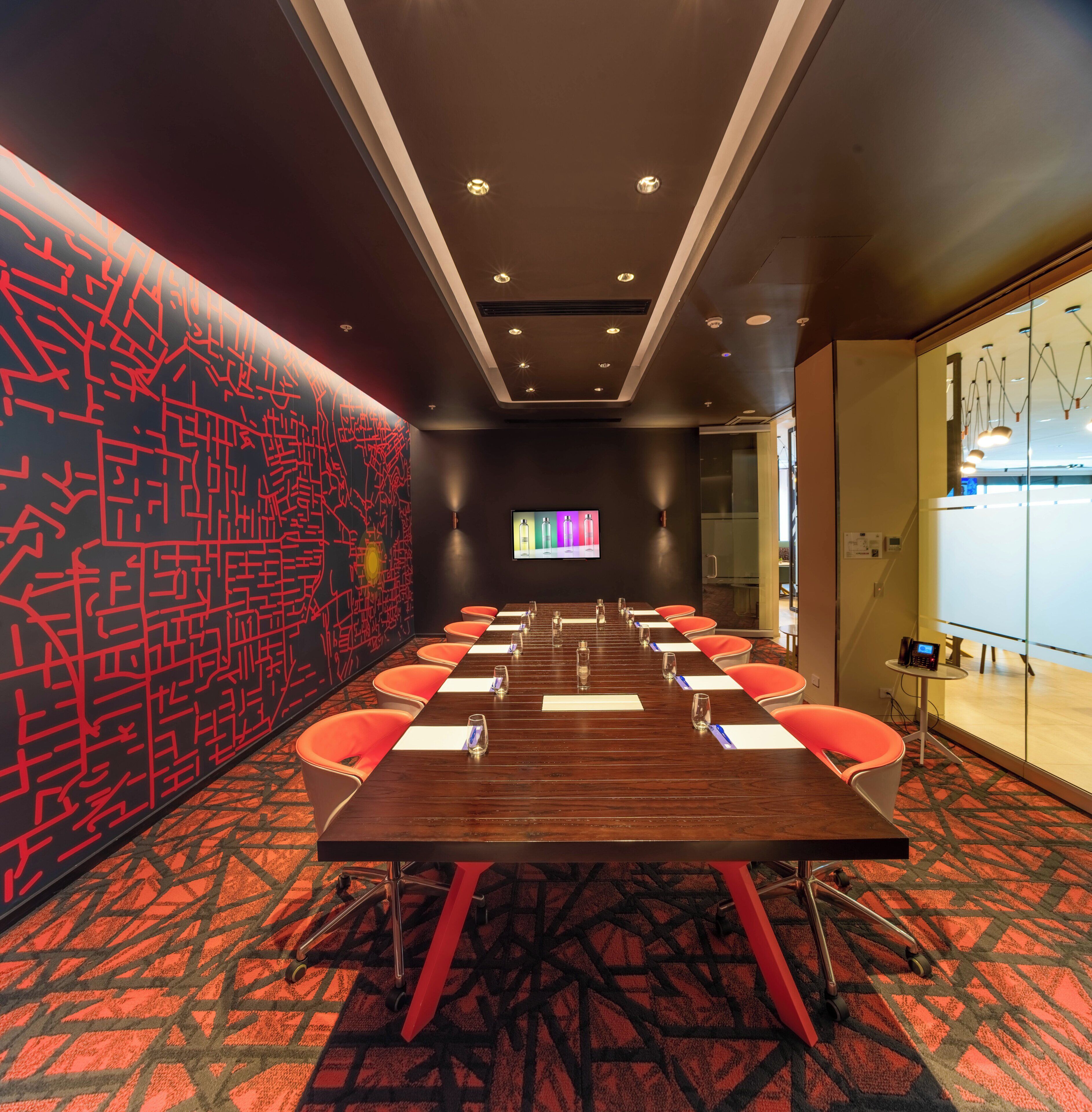 A conference room with a long table, chairs, and a screen.