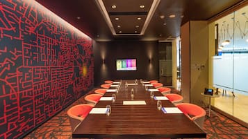 A conference room with a long table, chairs, and a screen.