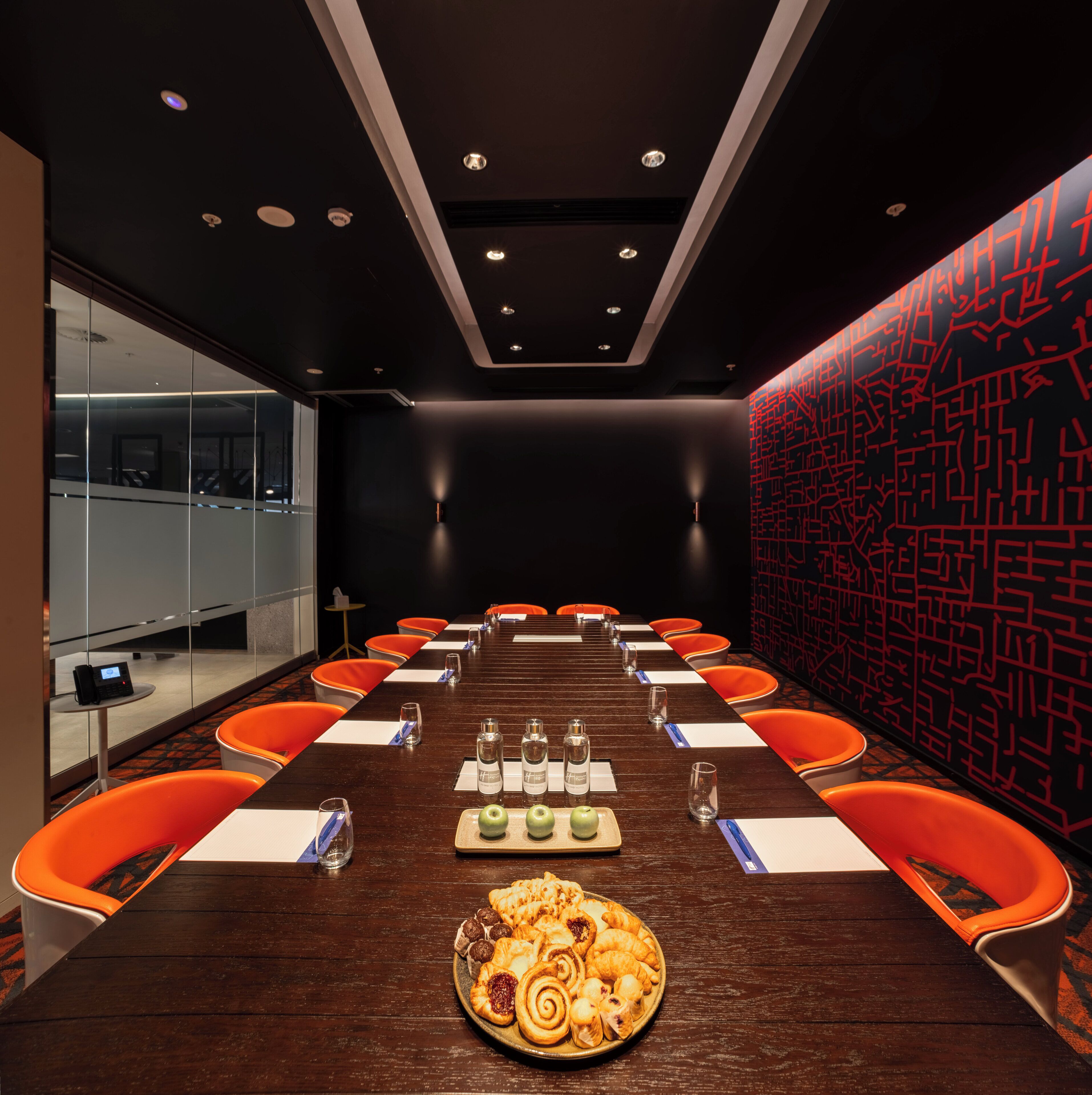A conference room with a long table, orange chairs, and a plate of pastries.