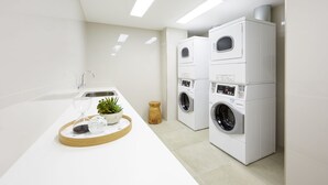 A modern laundry room with stacked washers and dryers, a sink, and a tray with a plant and glass. - Holiday Inn Express Adelaide City Centre by IHG (Adelaide)