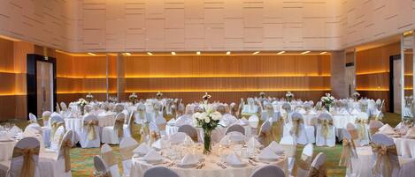 A banquet hall with round tables set for a formal event, featuring white tablecloths, gold sashes, and floral centerpieces.