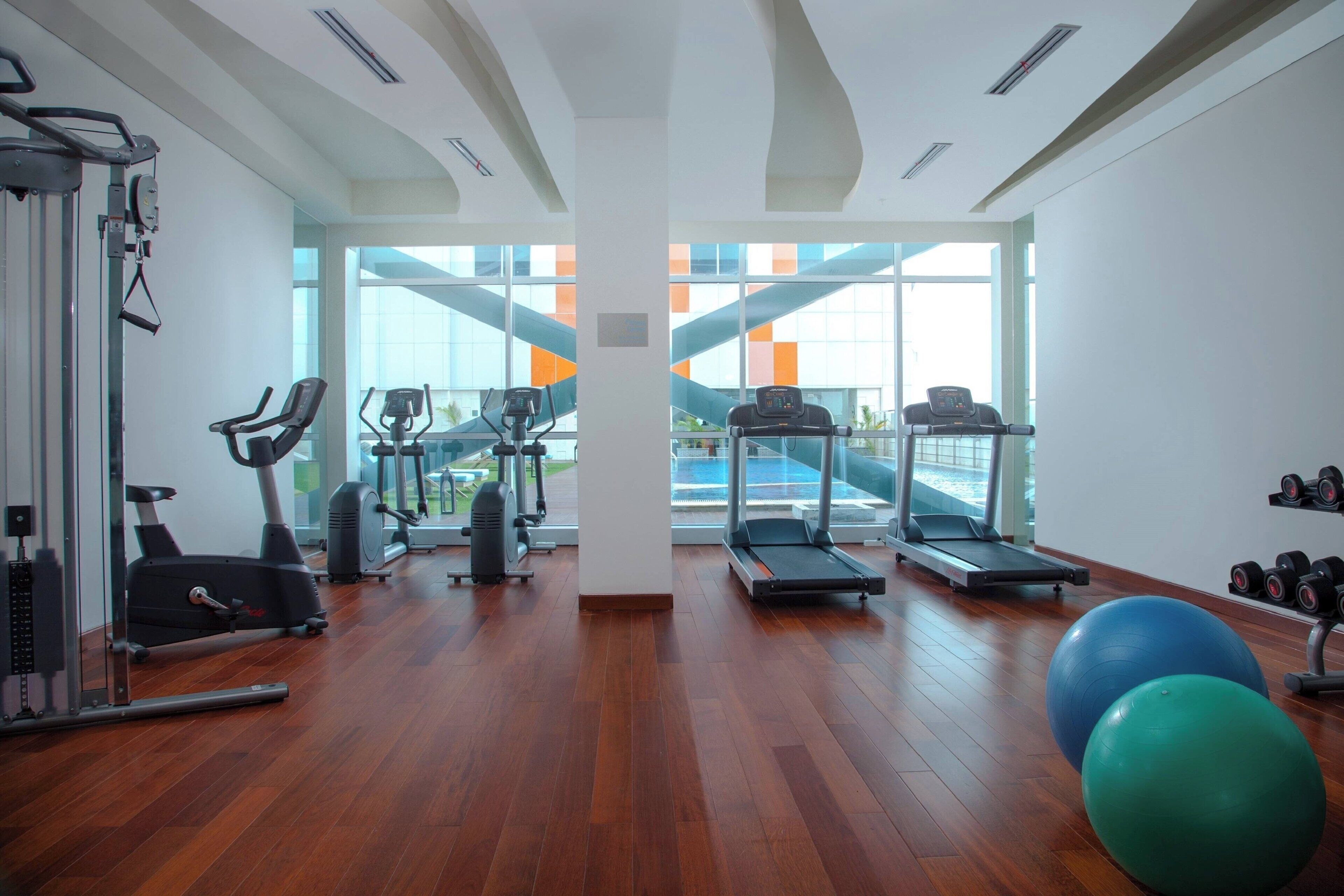 Ein Fitnessstudio mit Trainingsgeräten, großen Fenstern und Holzboden.