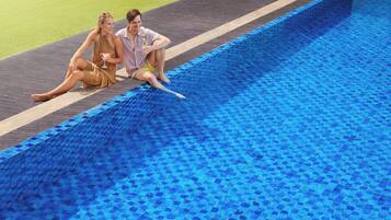 Dos personas sentadas junto a una piscina con borde de azulejos.