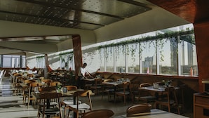 A modern restaurant with high ceilings, wooden chairs, and tables.