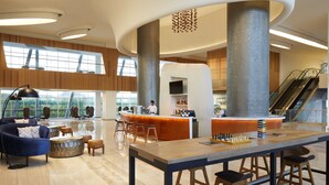 A spacious lobby with a central bar area, seating arrangements, and a large window providing natural light.