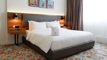 A hotel room with a large bed, two bedside tables, a nightstand, a digital clock, and a wall-mounted lamp.