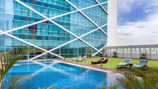 A modern hotel with a large glass facade, a swimming pool, and outdoor seating areas.