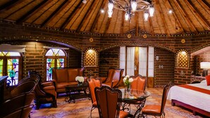 A cozy room with a wooden ceiling, a bed with red pillows, a dining table with chairs, and a stained glass window.