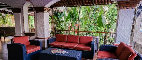 A covered outdoor seating area with wicker furniture and a red cushioned sofa.