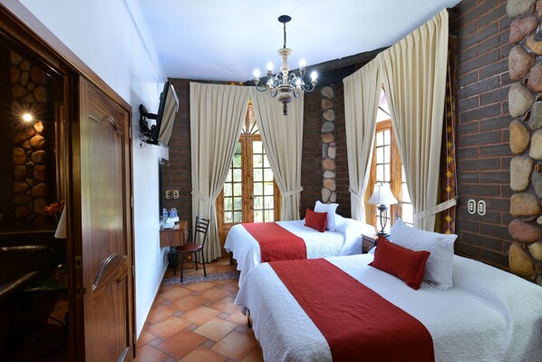 Habitación de hotel con dos camas, una pared de piedra, una araña y una puerta de madera.