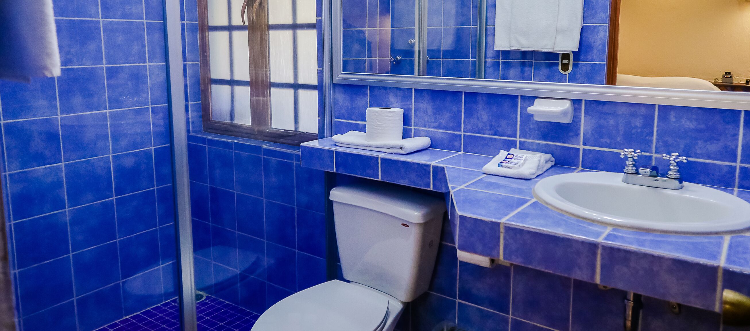 Un baño con azulejos azules, inodoro blanco, lavamanos y espejo.