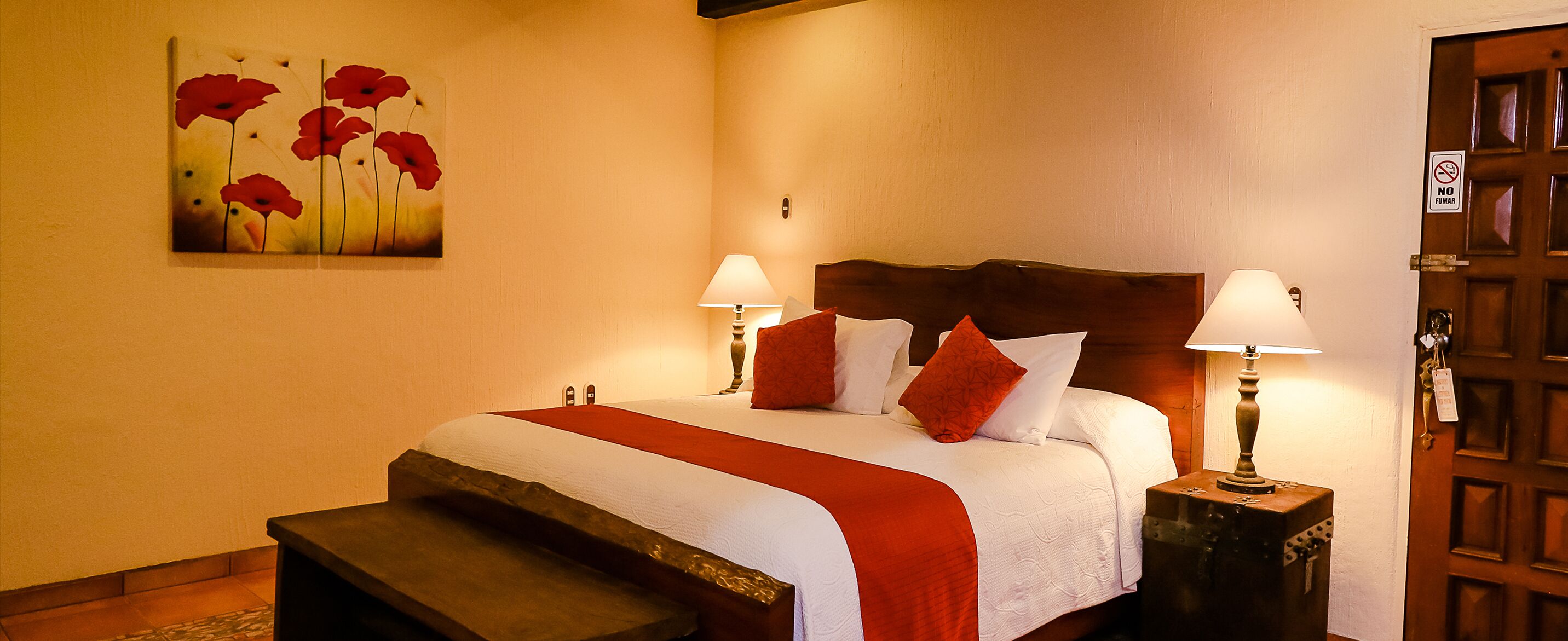 A neatly made bed with a red and white bedspread, two bedside lamps, and a wooden headboard.