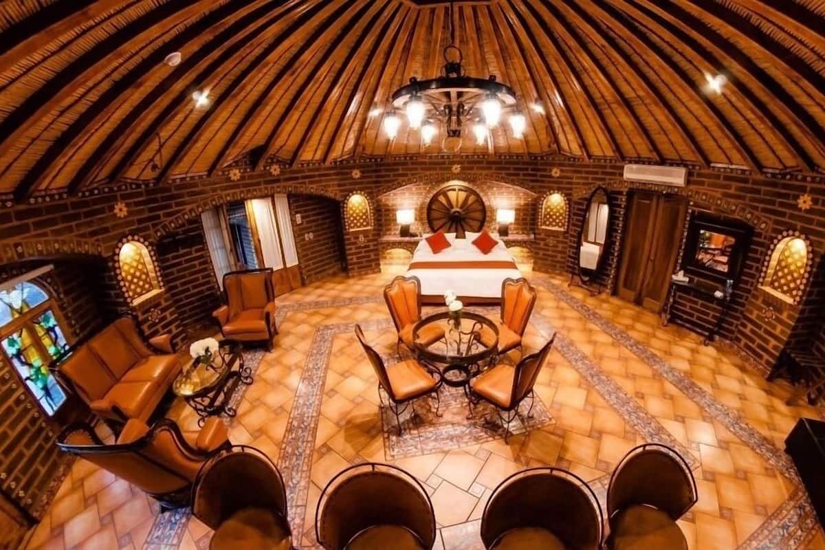 Una habitación acogedora y circular con una cama grande, varios rincones de descanso y un techo distintivo en forma de cúpula de madera.