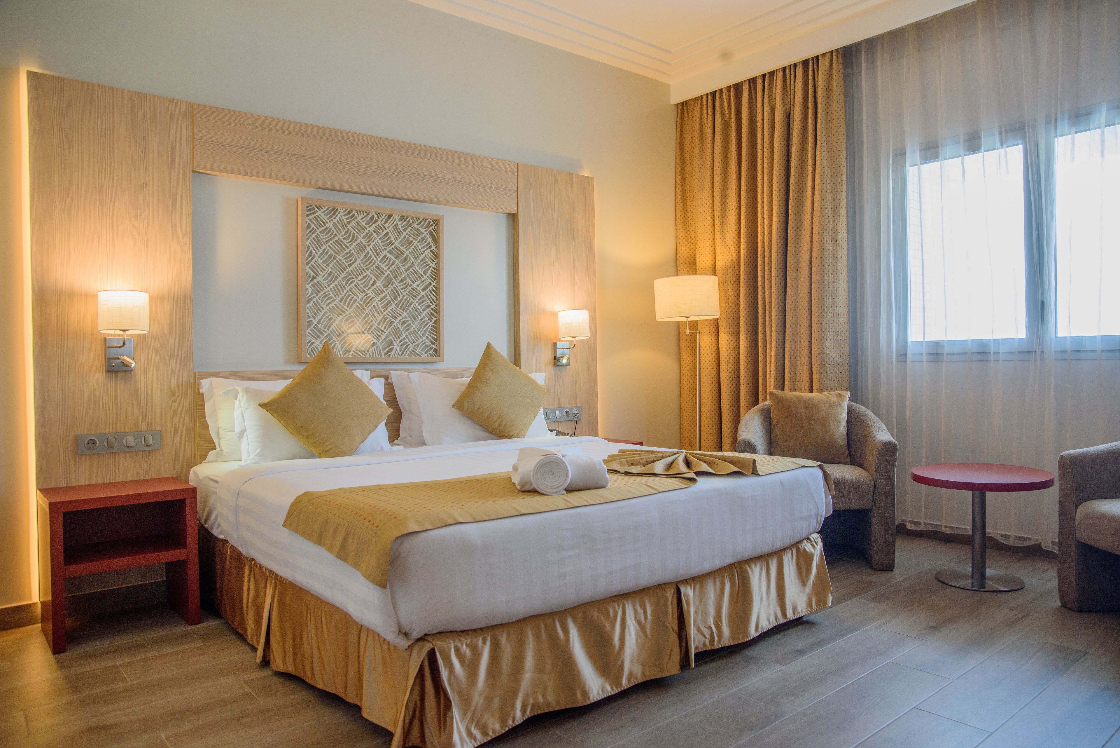 Habitación de hotel con una cama grande, dos lámparas de noche, una mesita y una silla.
