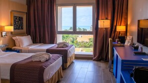 A hotel room with two beds, a desk, and a large window with curtains. - Golden Tulip Le Diplomate Cotonou (Cotonou)