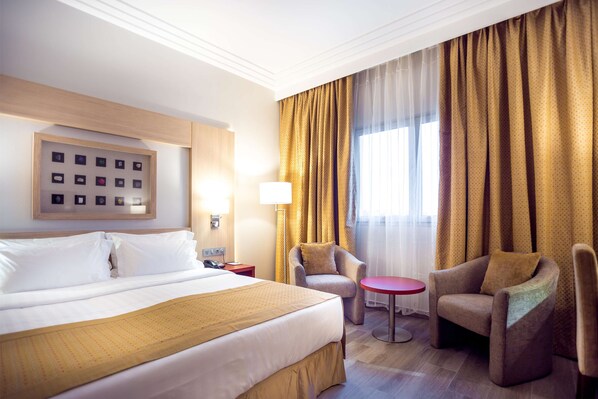 A hotel room with a large bed, two armchairs, a small table, and a framed photo collage on the wall. - Golden Tulip Le Diplomate Cotonou (Cotonou)