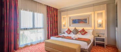 A hotel room with a large bed, a bench, a nightstand, and a painting on the wall.