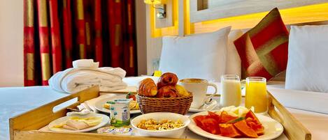 A breakfast tray with croissants, yogurt, fruit, and juice on a hotel bed.