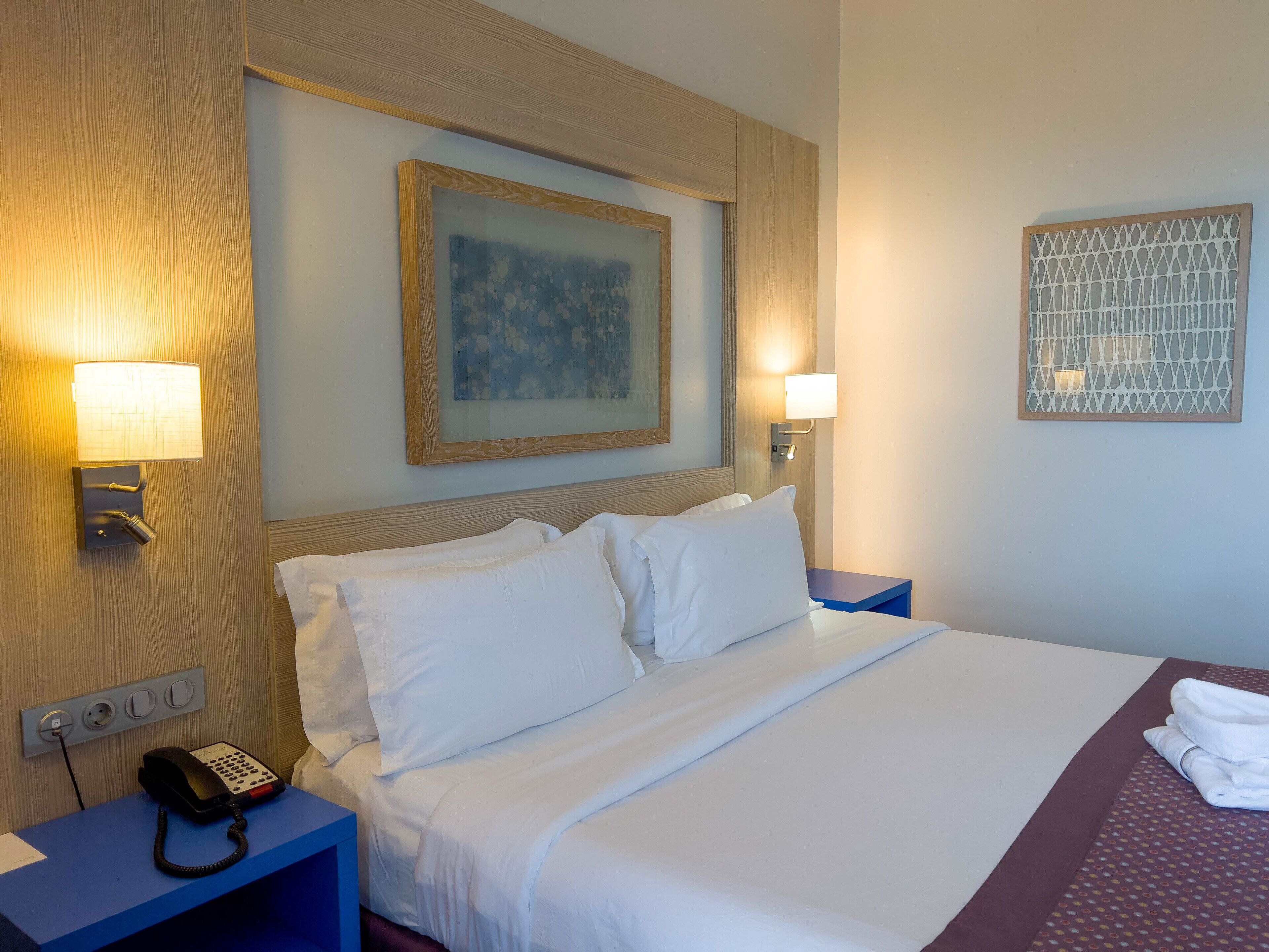 A hotel room with a bed, two bedside tables, a telephone, and wall-mounted lamps.