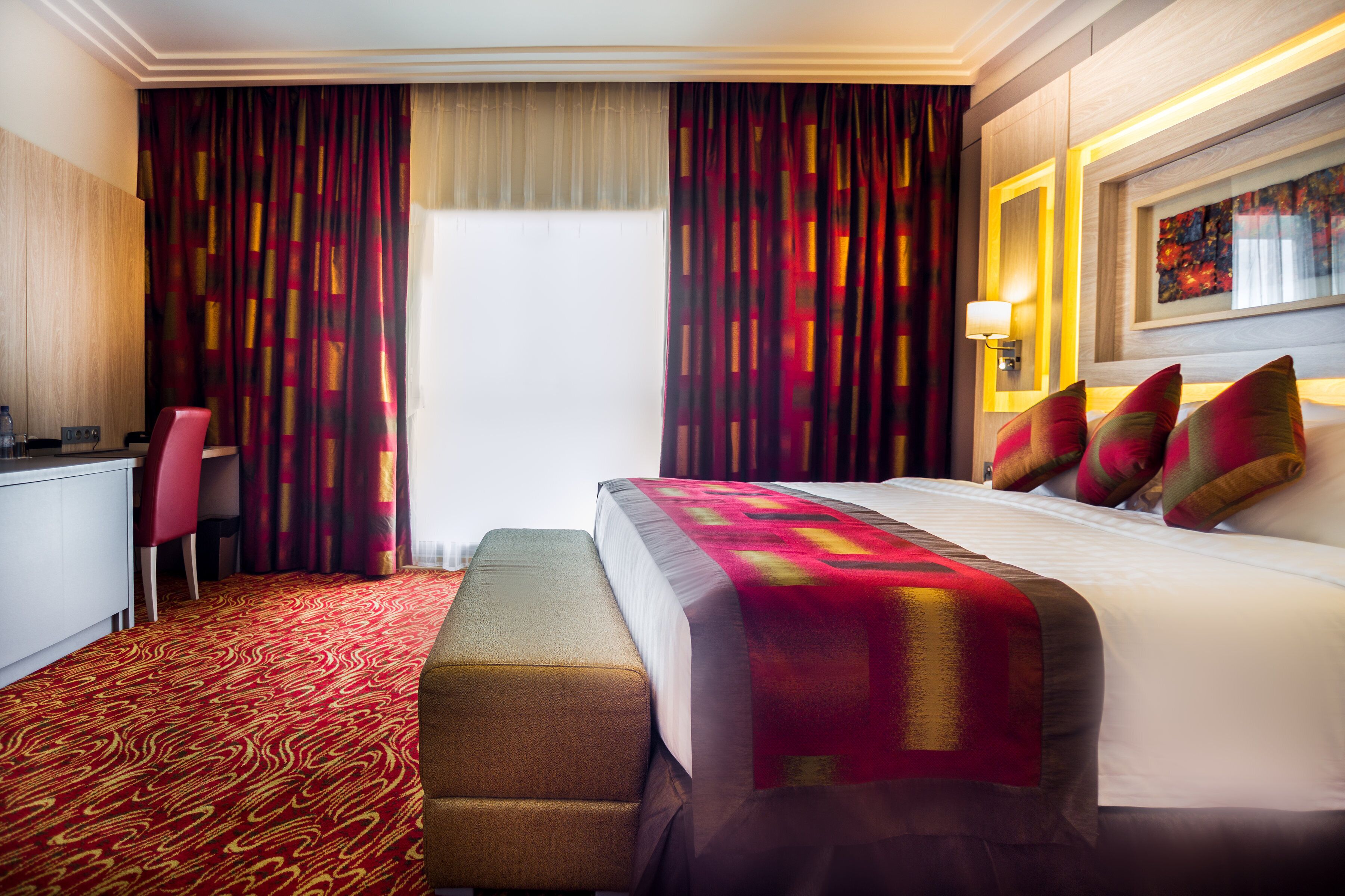 A hotel room with a large bed, a desk, a chair, and a bench.