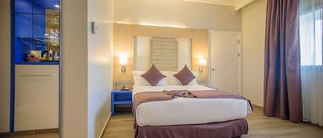 Habitación de hotel con una cama grande, mesitas de noche, un armario y un baño visible a través de una puerta de cristal.