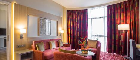 A hotel room with a red carpet, a sofa, a chair, a small table, and a lamp.