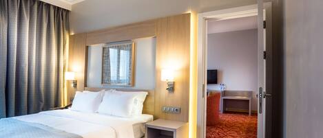 Una habitación de hotel con una cama, mesitas de noche, una lámpara, un televisor y una puerta que da a otra habitación.