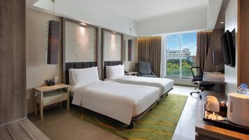 A hotel room with two beds, a desk, a chair, a TV, and a view of the city.
