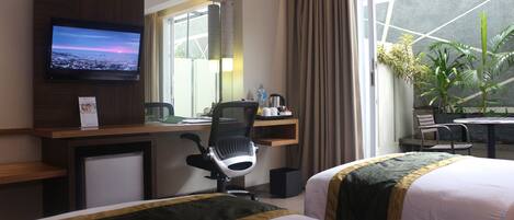 Una habitación de hotel con cama, escritorio con silla, televisión y ventana con cortinas.