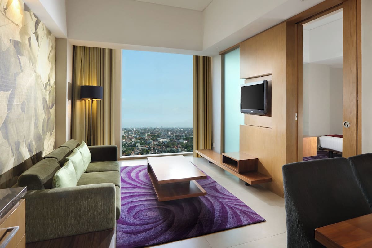Ett modernt hotellrum med utsikt över staden, en soffa, ett soffbord, en TV och ett träskåp.