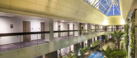 A hotel interior with a central pool, multiple floors, and a glass ceiling.