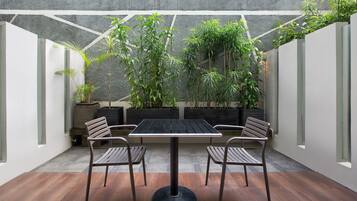 Un patio con una mesa y sillas, rodeado de plantas en macetas y un muro de hormigón.
