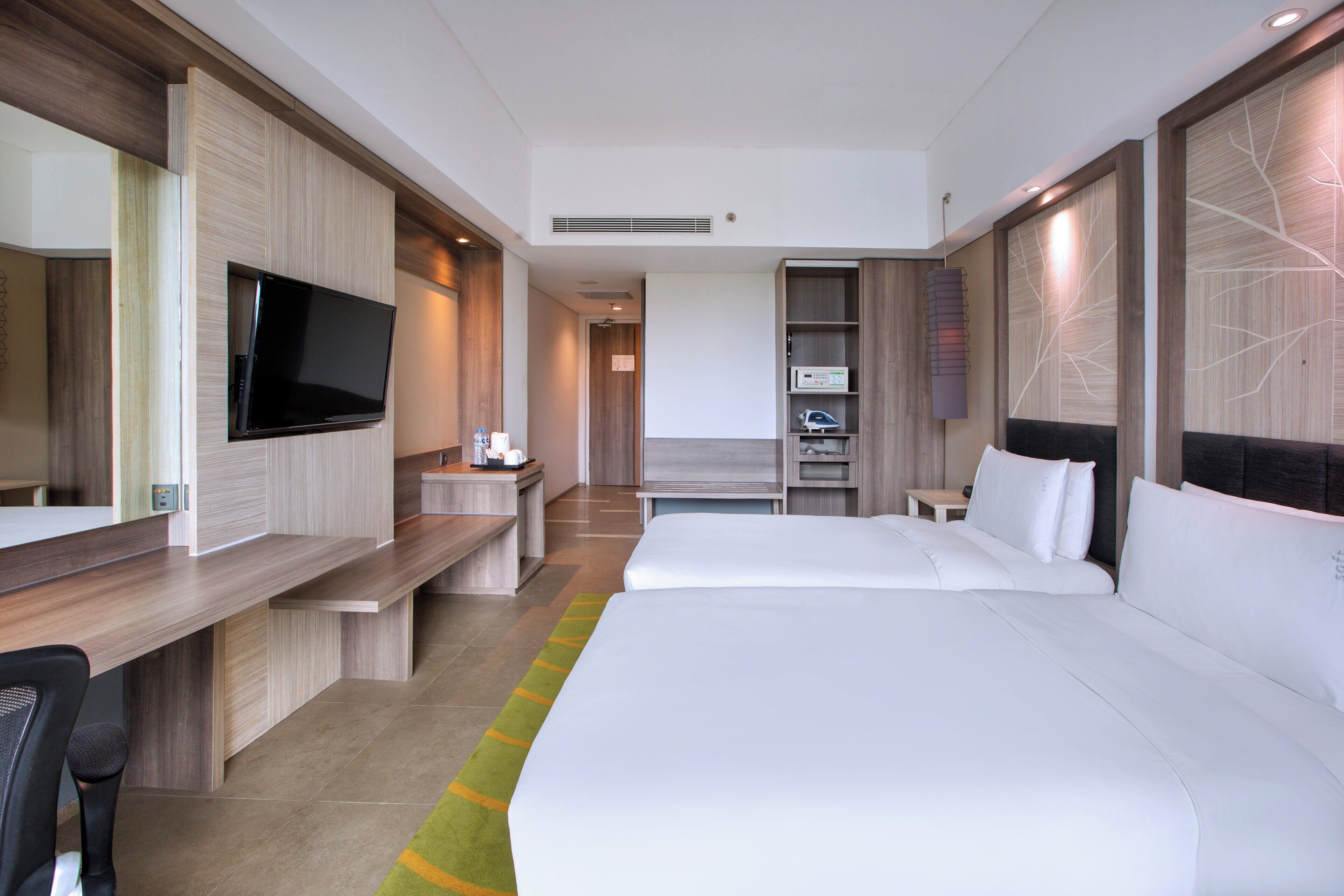 A modern hotel room with a large bed, a desk with a flat-screen TV, a minibar, and a seating area with a sofa and chairs.