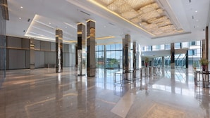 Um hall amplo com piso de mármore polido, grandes janelas e luminárias modernas.